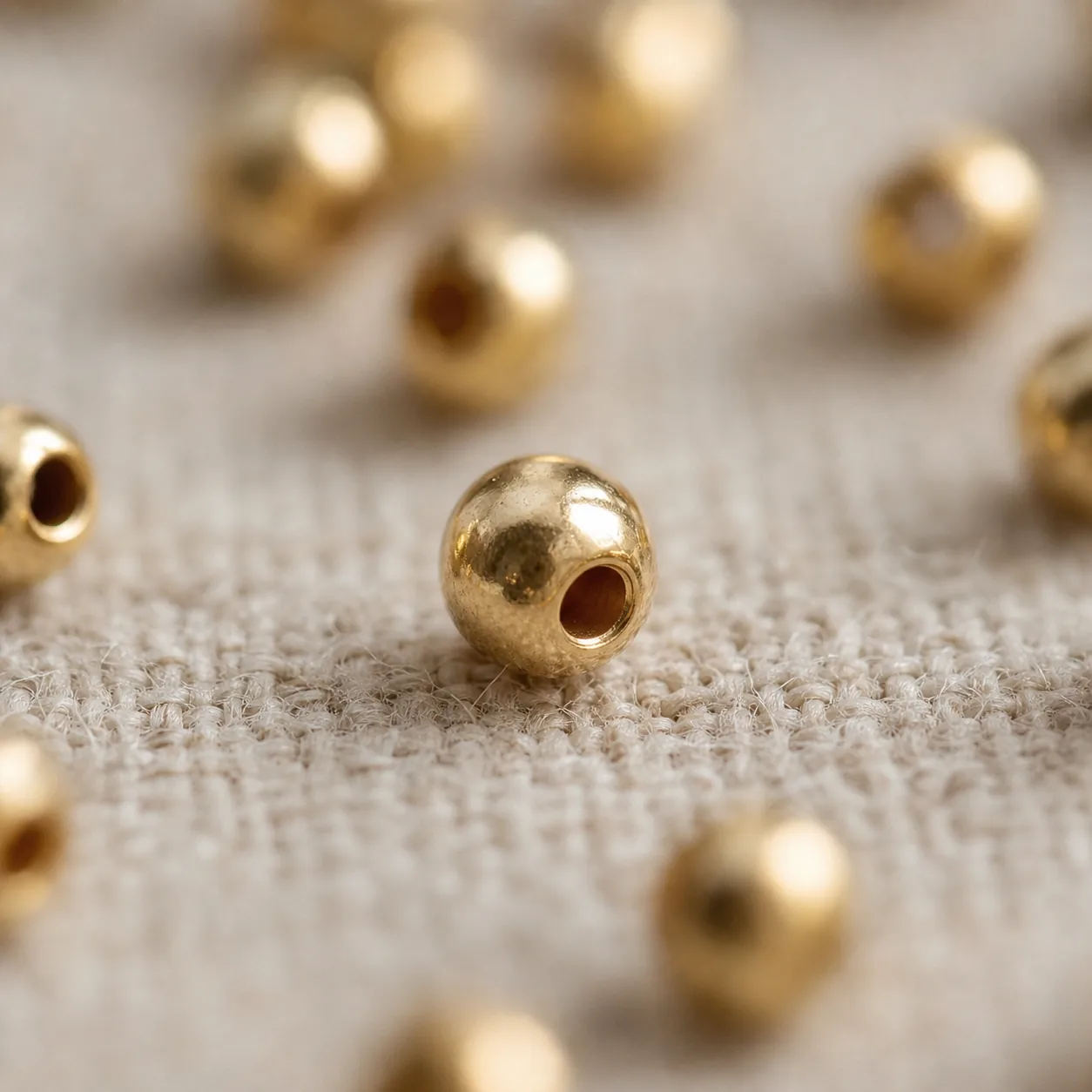 Detalle macro de una bola de oro laminado 18k con su perforación, sobre tela de lino